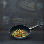 Black frying pan with vegetables on a dark textured background