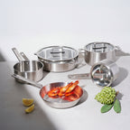 Set of stainless steel cookware with a pan containing shrimp on a light background